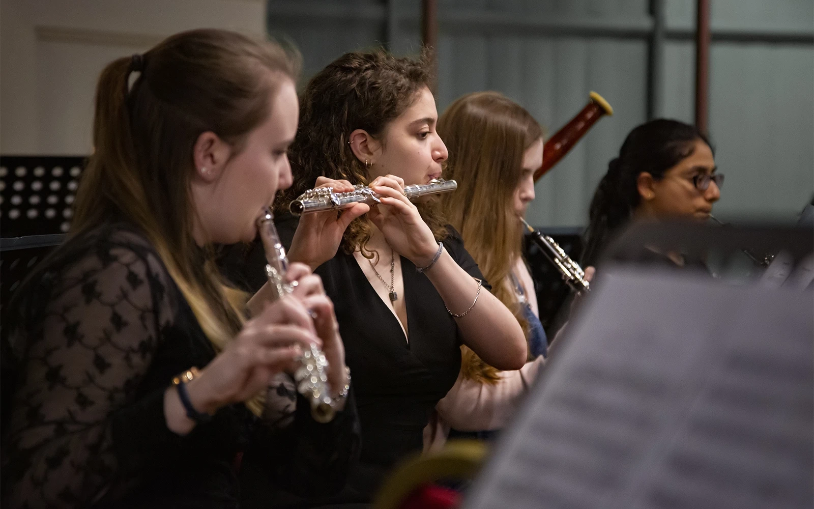 Several young women playing instruments in the woodwind section of the orchestra