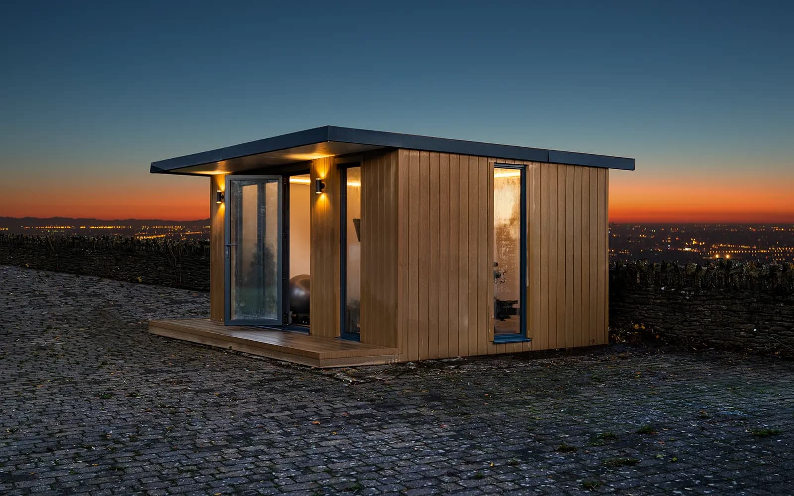 A garden room front on with a paved courtyard at dusk