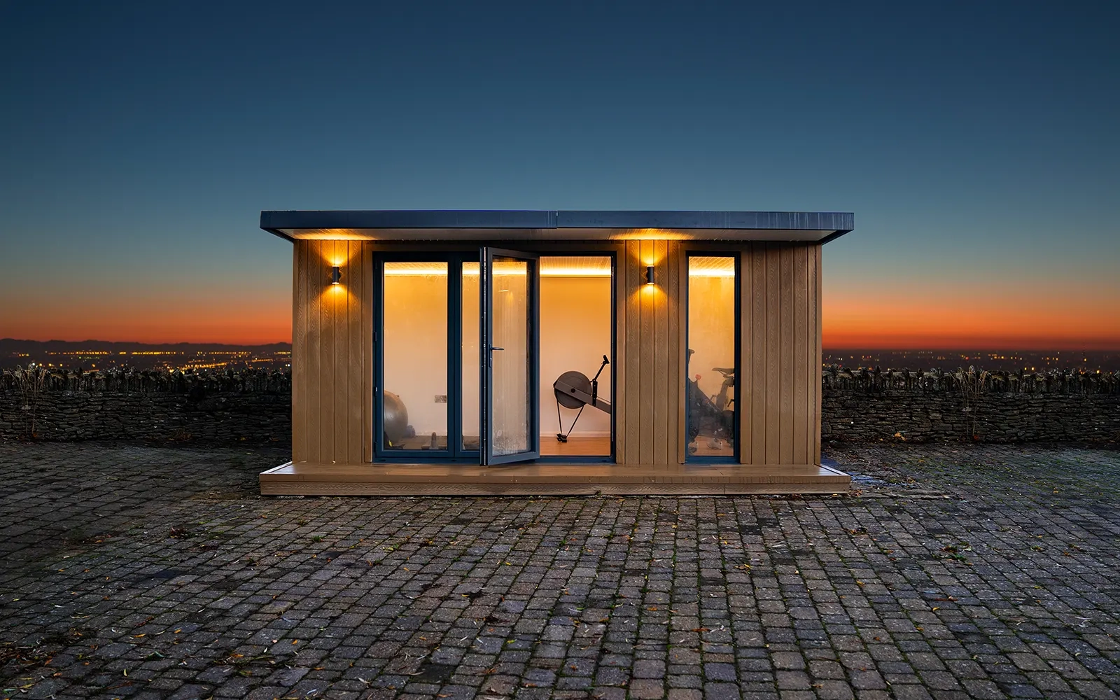 A garden room front on with a paved courtyard at dusk