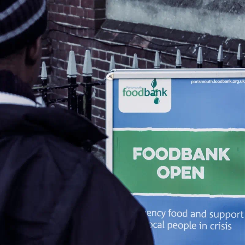 A gritty still from the Portsmouth Food Bank short documentary, taken over the shoulder of a food bank user staring at the foodbank ‘open’ sign