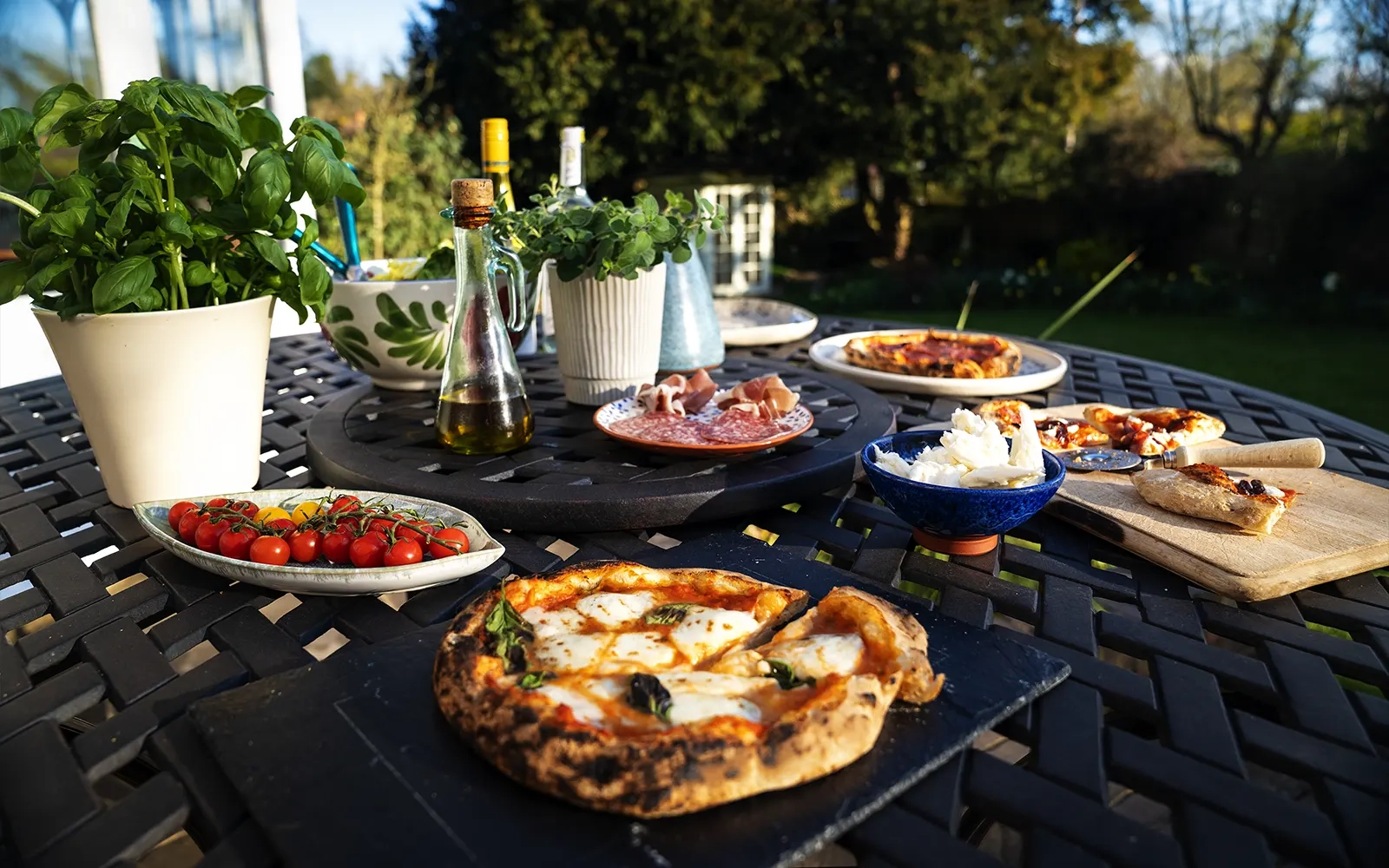 Wide angle of an outdoor table with various pizzas, condiments and salads set out beautifully