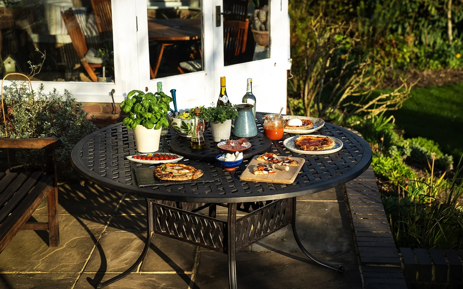 Outdoor table with various pizzas, sauces and pot plants