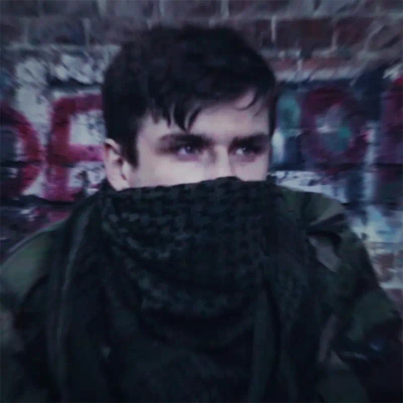 A young man in an urban setting, face half-covered by a scarf, a still from the ‘Abandoned’ title sequence