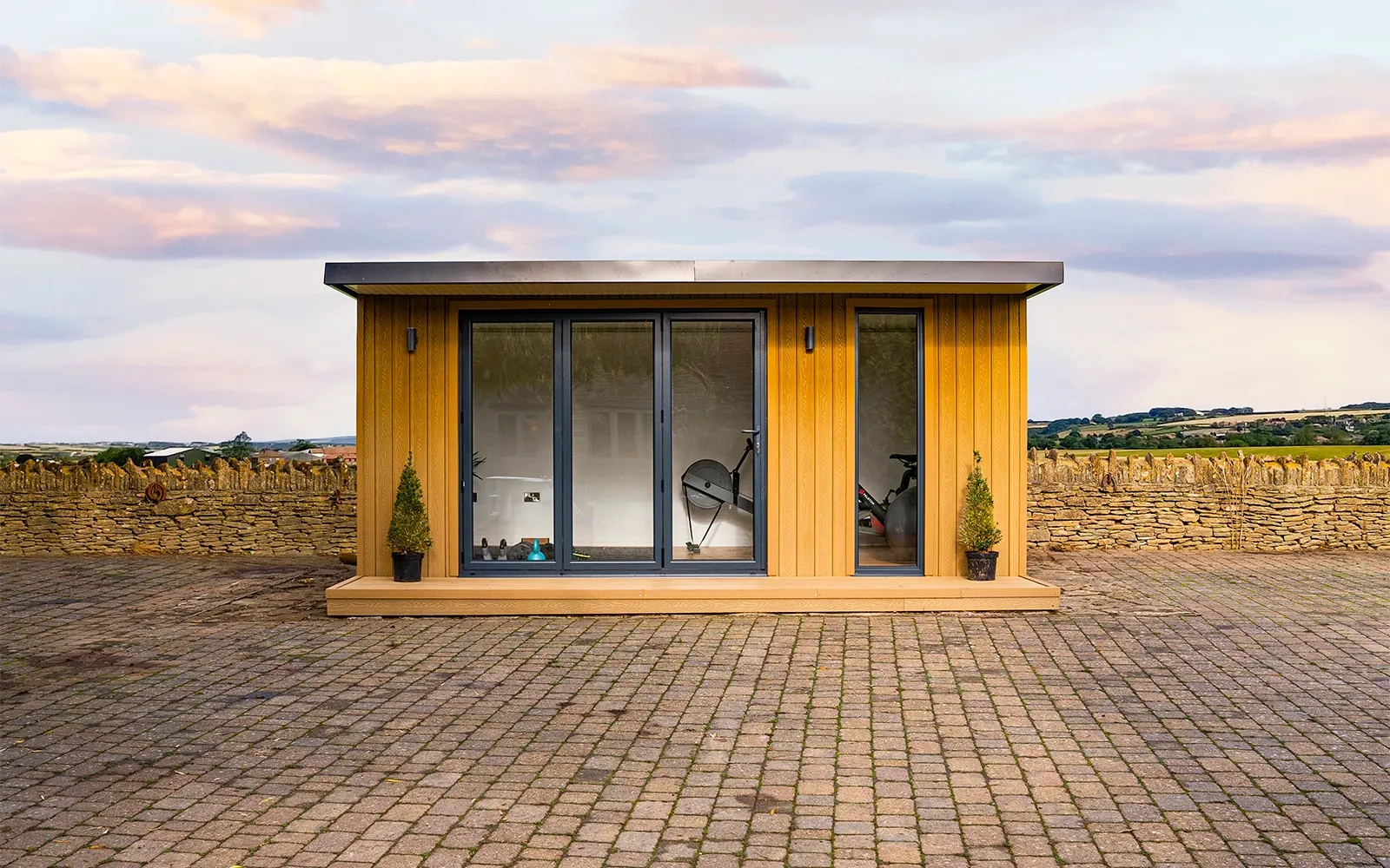 A garden room front on with a paved courtyard and a faint sunset in the background