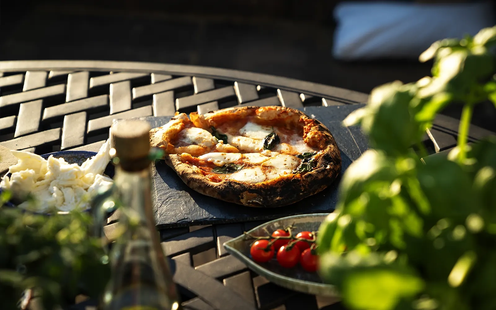 Close-up of a pizza on an outdoor table surrounded by a plant and sauces