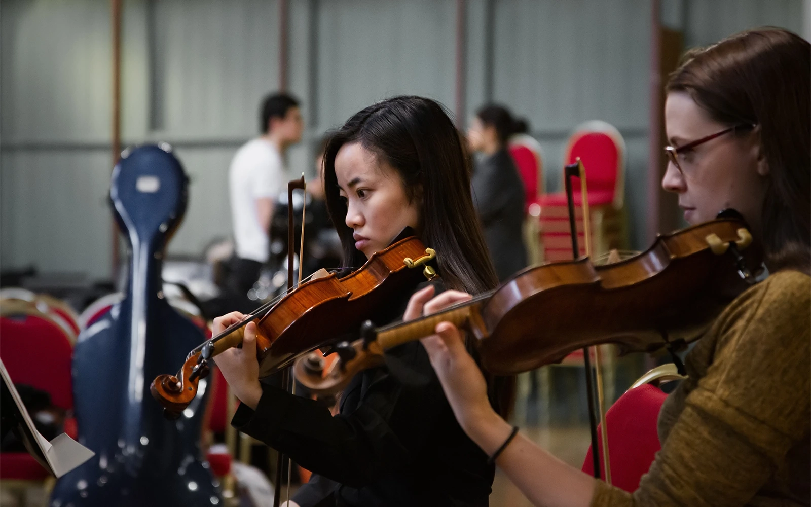 Two young women women playing violins during concert rehearsals