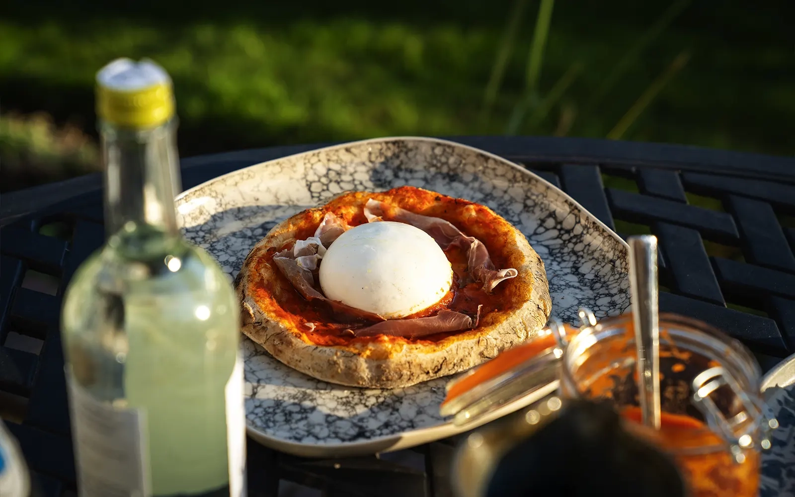 Close-up of a pizza on an outdoor table with a wine bottle in the foreground
